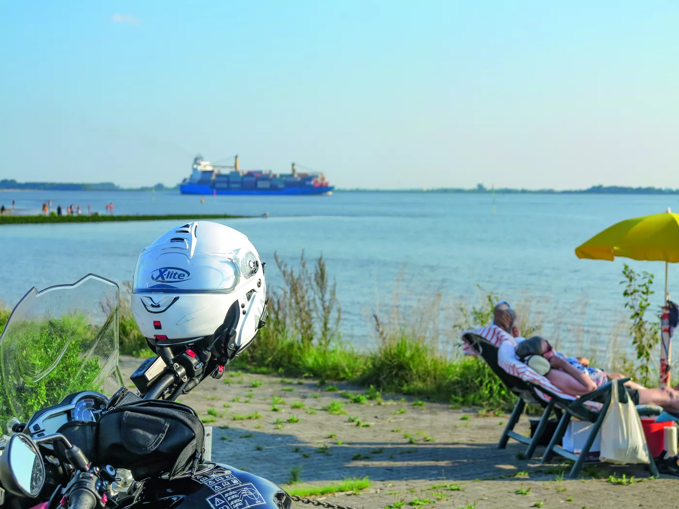 Motorrad am Ufer, im Hintergrund zieht ein Frachtschiff vorbei Motorrad am Ufer, im Hintergrund zieht ein Frachtschiff vorbei
